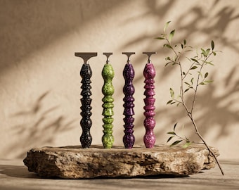 May include: Four safety razors with textured, speckled handles in black, lime green, purple, and magenta. Each razor features a metallic head and a distinctively contoured, multi-ribbed handle design, standing upright on a rough, natural stone surface.