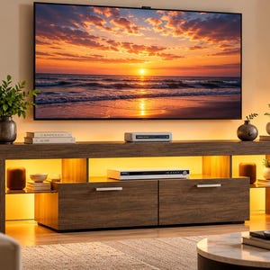 May include: A long, dark wood media console featuring two central drawers with silver handles, open side shelving, and integrated warm yellow LED lighting. A large flat-screen television displays a sunset beach scene above the console.