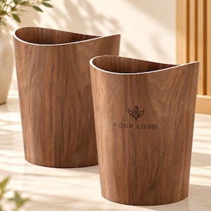 May include: Two cylindrical wastebaskets featuring a dark brown wood grain finish and a curved, wave-like top rim. The front-most wastebasket displays a small, dark brown icon of three leaves above the text YOUR LOGO centered on its exterior surface.