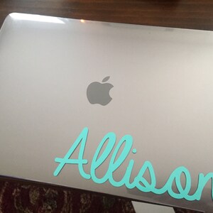 Op de afbeelding: Een zilveren laptop met het Apple-logo en de naam "Allison" in turquoise op de deksel.