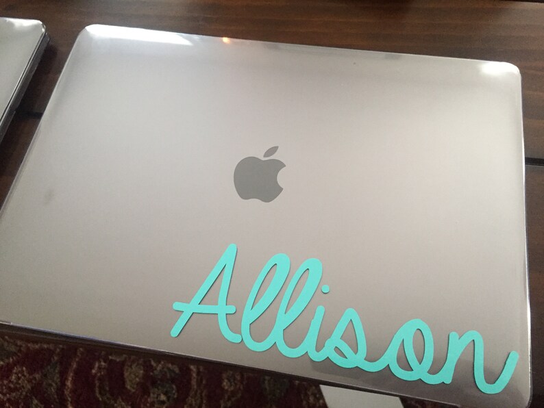 Op de afbeelding: Een zilveren laptop met het Apple-logo en de naam "Allison" in turquoise op de deksel.