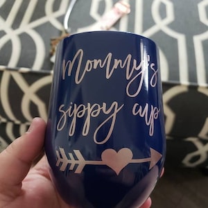 May include: A navy blue stainless steel tumbler with a rose gold arrow and heart design. The tumbler has the text "Mommy's sippy cup" written on it.