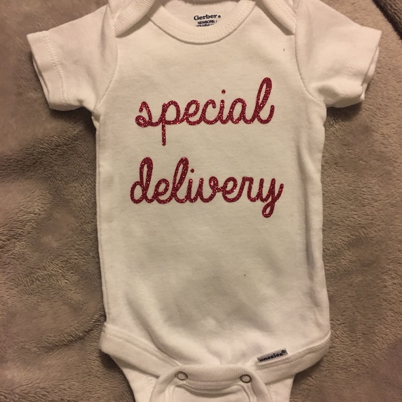 K&ouml;nnte beinhalten: Wei&szlig;er Baby-Strampler mit dem Schriftzug "special delivery" in roten Glitzerbuchstaben.