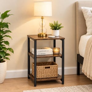 May include: A three-tier side table with a dark wood grain finish and a black metal frame. The top surface holds a glass lamp with a white shade, a small potted green plant, and a coaster. The middle shelf holds two books and a candle.
