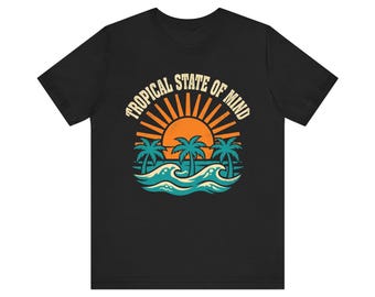 May include: A black short-sleeve t-shirt featuring a graphic print of an orange sun rising over teal ocean waves and palm trees. The text TROPICAL STATE OF MIND is printed in a cream-colored arched font above the sun and palm tree illustration.