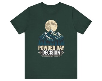 May include: A dark green short-sleeve t-shirt featuring a graphic of a full moon over snow-capped mountains and a forest. Below the mountains, the text reads "POWDER DAY DECISION" in a distressed white font, accented by small decorative arrows.