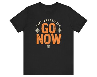 May include: A black short-sleeve t-shirt featuring a graphic design in orange and cream. The text reads "LIVE UNSCRIPTED" in an arc above "GO NOW" in large, bold letters. The design includes three small compass rose icons in cream.