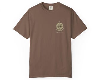 May include: A brown short-sleeve t-shirt featuring a small graphic on the left chest. The graphic depicts a beige compass rose with the text "upontide" printed underneath in a simple, lowercase font. The shirt has a crew neckline and a standard fit.