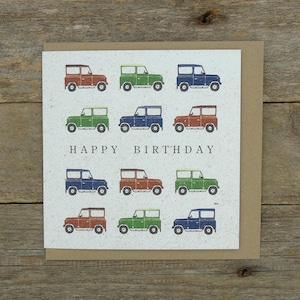 Könnte beinhalten: Geburtstagskarte mit beigem Hintergrund. Sie zeigt ein Raster von Illustrationen von Autos im Vintage-Stil in Rot, Grün und Blau. Die Worte "HAPPY BIRTHDAY" sind in Schwarz gedruckt. Die Karte liegt auf einem braunen Umschlag.