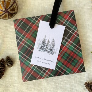 May include: A red, green, and black plaid gift wrap with a white gift tag. The gift tag has a black and white illustration of three pine trees and the text "merry christmas, the wilsons".