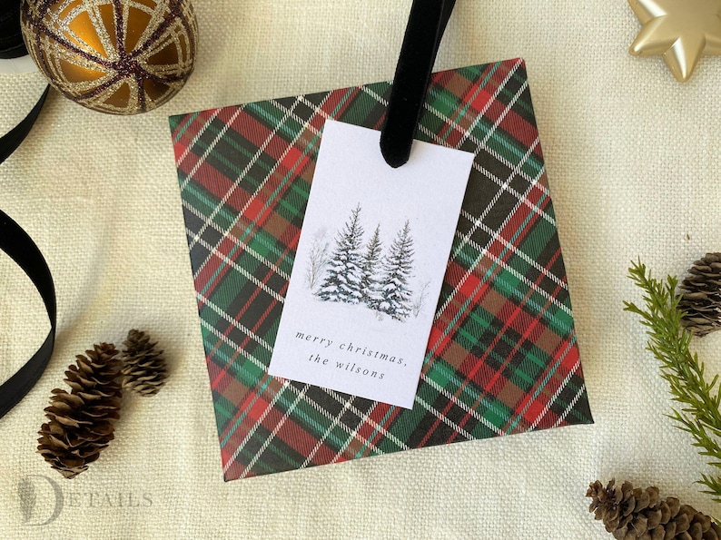 May include: A red, green, and black plaid gift wrap with a white gift tag. The gift tag has a black and white illustration of three pine trees and the text "merry christmas, the wilsons".