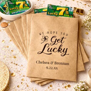 Puede incluir: Un montón de bolsas de papel marrón con la frase "We Hope You Get Lucky" impresa en negro. Las bolsas contienen boletos de lotería. Los nombres "Chelsea & Brennan" y la fecha "9.22.XX" también están impresos en las bolsas.