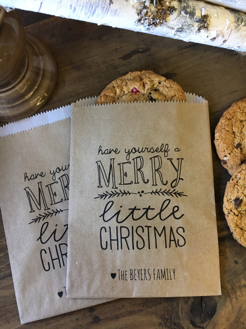 May include: Two brown paper bags with the text "have yourself a merry little christmas" and a heart with "The Beyers Family" printed on them. The bags are filled with cookies.