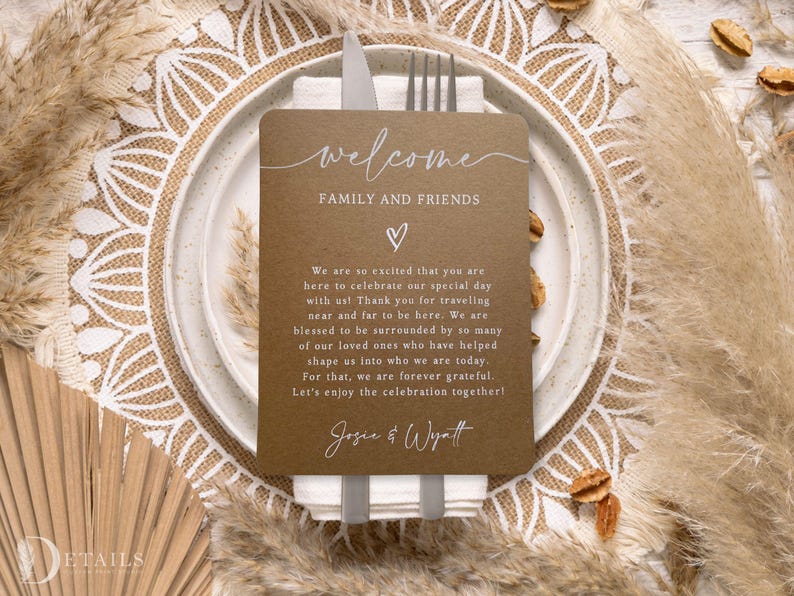 K&ouml;nnte beinhalten: Ein Gedeck mit einer braunen Willkommenskarte mit der Aufschrift "welcome FAMILY AND FRIENDS" und einem Herzsymbol. Die Karte liegt auf einer wei&szlig;en Serviette mit Gabel und Messer. Das Gedeck befindet sich auf einem dekorativen Teller mit getrockneten Pflanzen.