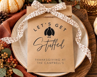 May include: A rectangular brown paper bag tied with a white ribbon featuring a small brown floral pattern. The bag is printed with a black turkey icon, the text "LET'S GET Stuffed", and the text "THANKSGIVING AT THE CAMPBELL'S" in black ink.