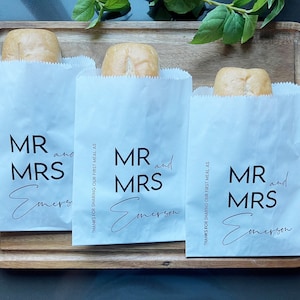 May include: Three white paper bags with the text "MR and MRS Emerson" printed on them. Each bag contains a small loaf of bread.