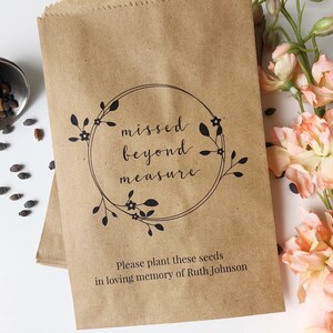 Può includere: Busta di semi di carta marrone con la scritta "missed beyond measure" all'interno di una ghirlanda floreale. Il fondo della busta recita "Please plant these seeds in loving memory of Ruth Johnson." Una tazza di metallo con semi e fiori rosa sono anche nell'immagine.