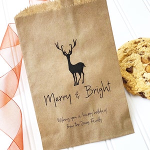 Pode incluir: Um saco de papel castanho com uma silhueta preta de uma rena e o texto "Merry & Bright" impresso nele. O saco também tem o texto "Wishing you a happy holiday! From the Jones Family" impresso nele.