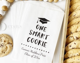 May include: White paper gift bags with black text that reads "One Smart Cookie" and a graduation cap graphic. The bags are personalized with the name "Gunnar Matthew Price" and the text "Class of 20xx".