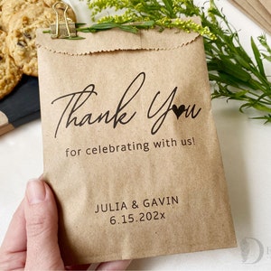 Op de afbeelding: Bruine papieren zak met een bedankbericht en een hartje. De zak zegt "Bedankt voor het vieren met ons!" en "JULIA & GAVIN 6.15.202x".