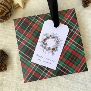 May include: A red, green, and black plaid gift bag with a white gift tag. The gift tag has a watercolor illustration of a pine cone wreath and the text "happy holidays, the Wilsons".