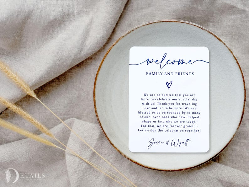 K&ouml;nnte beinhalten: Eine wei&szlig;e rechteckige Karte mit dem Wort "welcome" in marineblauer Schrift, zusammen mit dem Text "FAMILY AND FRIENDS" und einem Herzsymbol. Die Karte liegt auf einem wei&szlig;en Teller mit braunem Rand, auf einer beigen Leinenoberfl&auml;che.