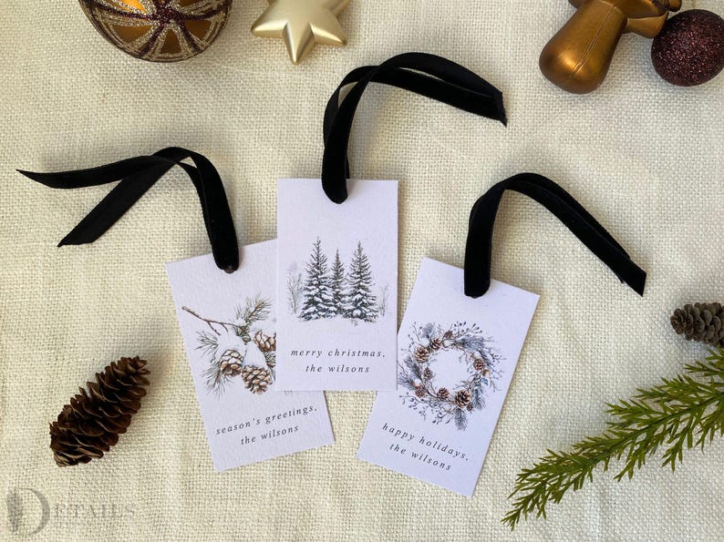 May include: Three white gift tags with black ribbon. The tags feature watercolor illustrations of pine trees, a wreath, and pine cones. The text on the tags reads "merry christmas, the wilsons", "season's greetings, the wilsons", and "happy holidays, the wilsons".