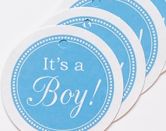 May include: A stack of round gift tags with a light blue center and white border. The text "It's a Boy!" is printed in a script font. Each tag has a small hole at the top for attaching to a gift.