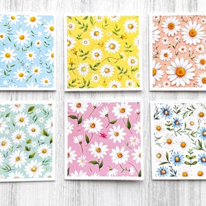 May include: Six square cards with daisy floral patterns. Each card features a different background color: light blue, yellow, peach, mint green, pink, and white. The daisies have white petals and yellow centers, with green leaves.