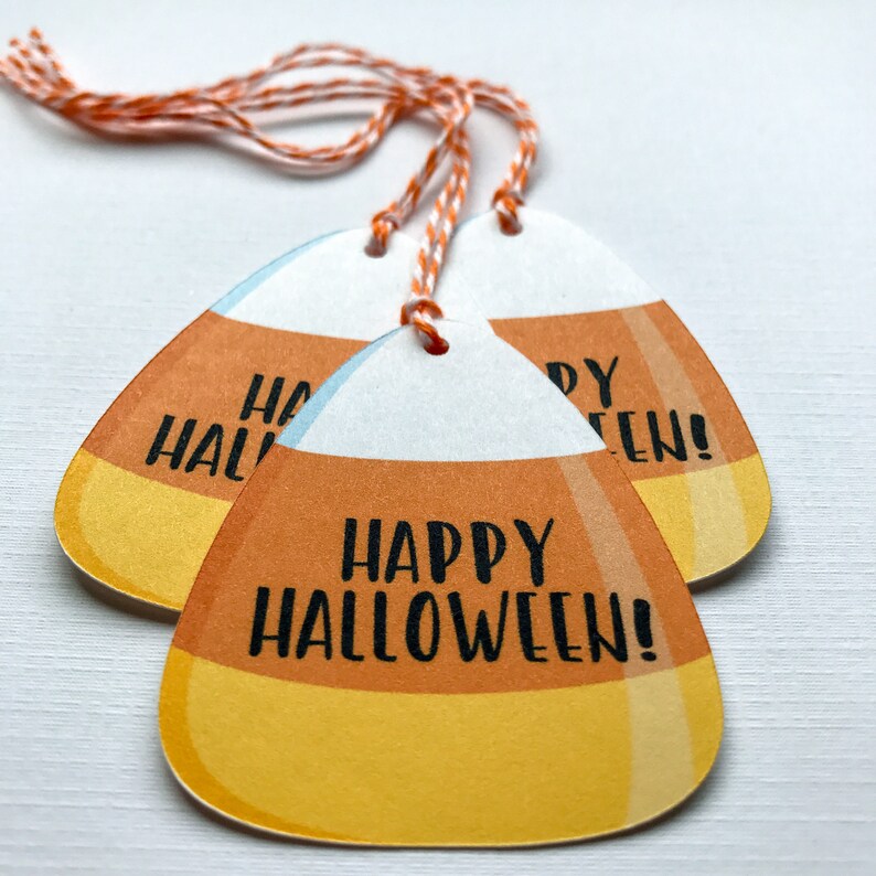 May include: Three orange, yellow, and white candy corn shaped gift tags with twine. The tags say "Happy Halloween!" in black text.