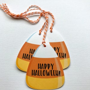May include: Three orange and yellow candy corn shaped gift tags with white twine. The tags have the text "Happy Halloween!" printed on them.