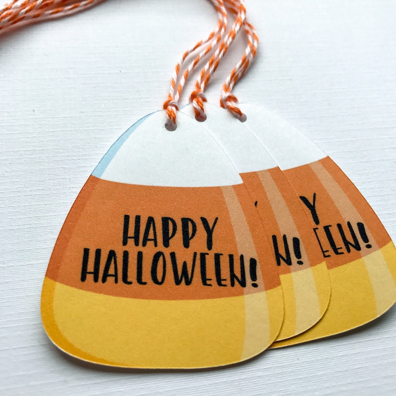May include: Three orange and yellow candy corn shaped gift tags with white string. The tags have the text "Happy Halloween!" and "Happy Halloween!" printed on them.