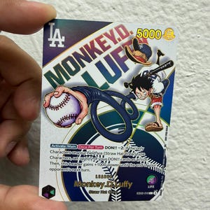 May include: A One Piece trading card featuring Monkey D. Luffy in a Los Angeles Dodgers uniform. The card displays the text Monkey D. Luffy, 5000 power, and game instructions. Luffy is shown stretching an arm to hold a baseball.