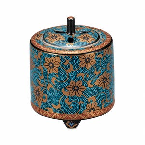 May include: A cylindrical ceramic incense burner featuring a vibrant turquoise background with a dense pattern of small dots and gold-colored floral motifs. The lid has a central black handle and cutouts, while the base rests on three small feet.