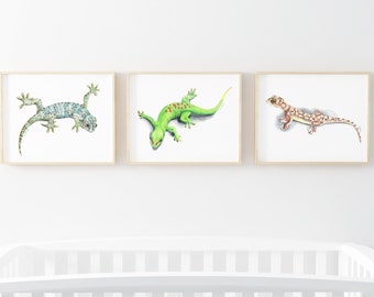 May include: Three framed watercolor paintings of geckos. The first gecko is green with blue spots and is lying on its belly. The second gecko is green with red spots and is lying on its belly. The third gecko is brown with white spots and is walking on all fours.