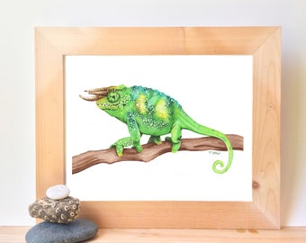 May include: A watercolour painting of a green chameleon with a long, curled tail, perched on a brown branch. The chameleon has a yellow stripe running down its back and a distinctive horn on its head. The painting is framed in a natural wood frame.