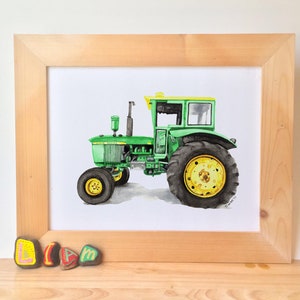 May include: A watercolor painting of a green John Deere tractor with yellow accents. The tractor is framed in a light wood frame.