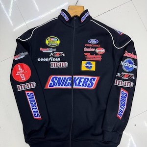 Könnte beinhalten: Eine schwarze Racing-Jacke mit Reißverschluss und verschiedenen gestickten Sponsorenlogos, darunter Snickers, M&M's, Ford Racing, NASCAR Nextel Cup Series, Coca-Cola, Skittles, Combos, Pedigree, Raybestos, SportClips, Goodyear und Robert Yates Racing.