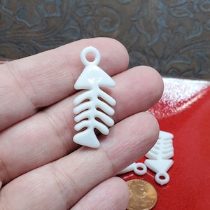 May include: White plastic fish bone charms with a loop at the top for hanging. The charms are about 1 inch long and are shown on a red surface.
