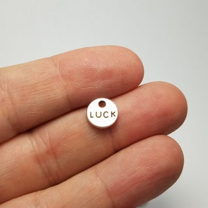 May include: A small, round, silver charm with the word "LUCK" engraved on it.