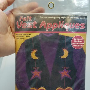 May include: A package of felt vest appliques with a purple vest on the front. The appliques include hearts, stars, and moons. The package includes iron-on patterns and optional no-sew instructions. The package is labeled "FashionArt by DIMENSIONS".
