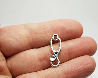 May include: Silver-toned metal charm shaped like a stethoscope. The charm has a loop at the top for attaching to a necklace or bracelet.