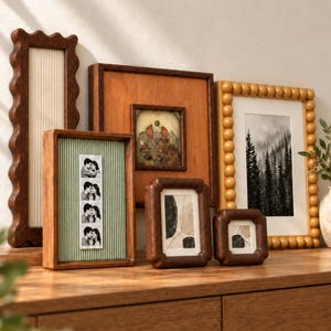 May include: A collection of five wooden picture frames in various shapes and sizes. One tall wavy frame, a square frame with a smaller inset, a rectangular frame with green striped backing, and two smaller frames with rounded edges and abstract art.