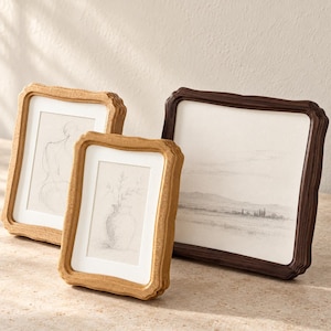 May include: Three picture frames with wavy, textured edges. Two frames are light brown and contain sketches of a figure and a vase with flowers. The third frame is dark brown and holds a landscape drawing of hills and trees.