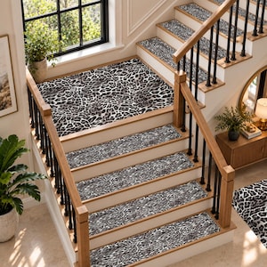 以下が含まれることがあります： 黒、白、グレーのヒョウ柄が施された長方形の階段用マットのセット。黒い金属製のバラスターと木製のハンドレールを備えた木製の階段に設置されており、各ステップの中央と踊り場を覆っています。