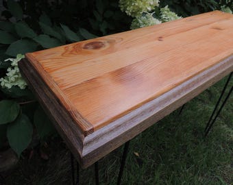 May include: A rectangular console table featuring a smooth, light-toned natural wood top with visible grain and knots. The table has a thick, weathered dark gray wooden frame edge and is supported by thin, black metal hairpin legs.