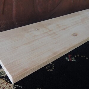 May include: A plain, light-colored wooden board with a smooth surface. The board is made of unfinished wood and has a natural grain pattern.
