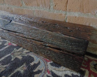 May include: A long, rectangular piece of dark brown reclaimed timber with a heavily weathered, rough, and textured surface. The wood features deep natural cracks, visible grain patterns, and a distressed finish throughout its length.