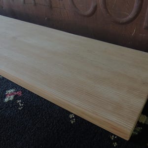 May include: A light brown wooden shelf with a smooth, slightly textured surface. The shelf is made of natural wood and has a light, natural finish.