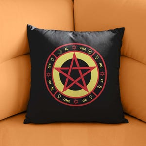 Può includere: Un cuscino quadrato nero con un design grafico centrale. Il motivo include una stella rossa a cinque punte all'interno di un cerchio giallo, circondata da un anello rosso contenente il testo ALPHA OMEGA, vari simboli planetari e piccole stelle.
